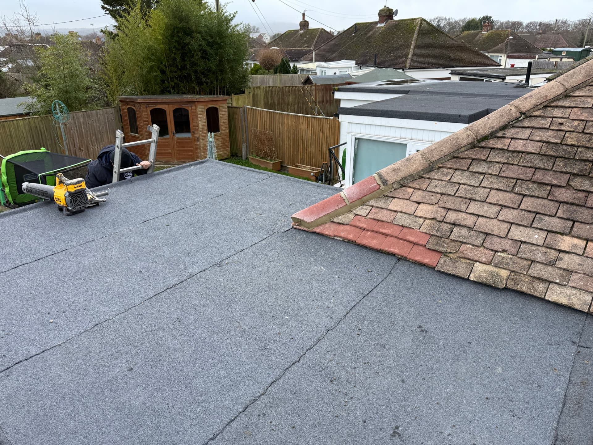 New grey mineral felt flat roof beside pitched tiles on a bungalow